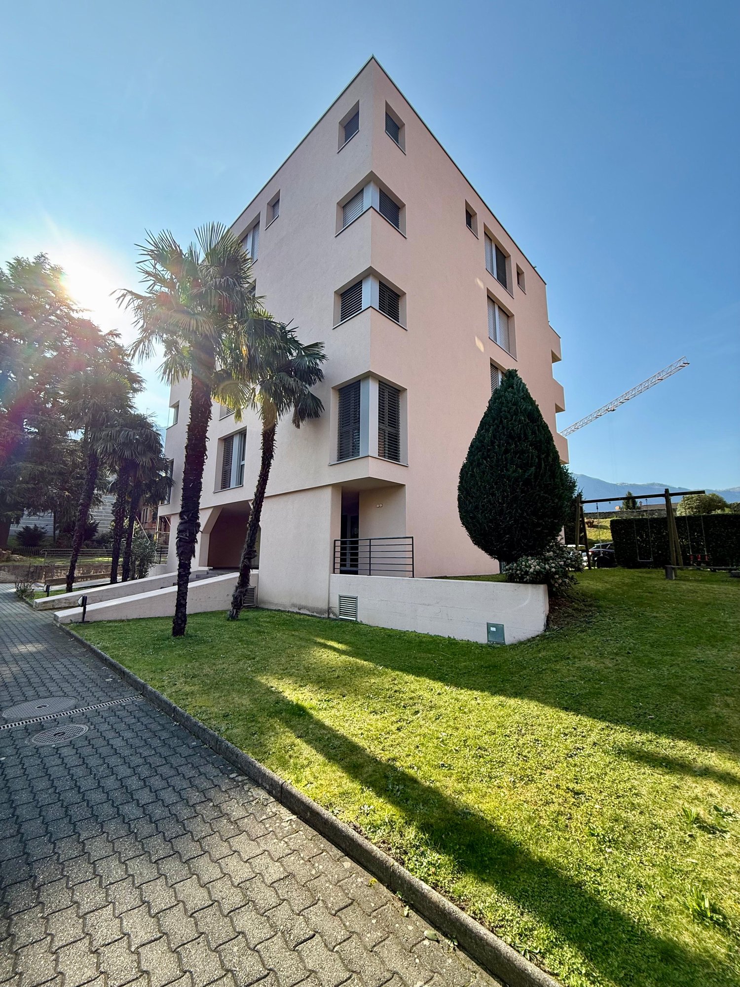 4 story apartment building, pink exterior, large windows, raised ground floor, palm trees, green lawn