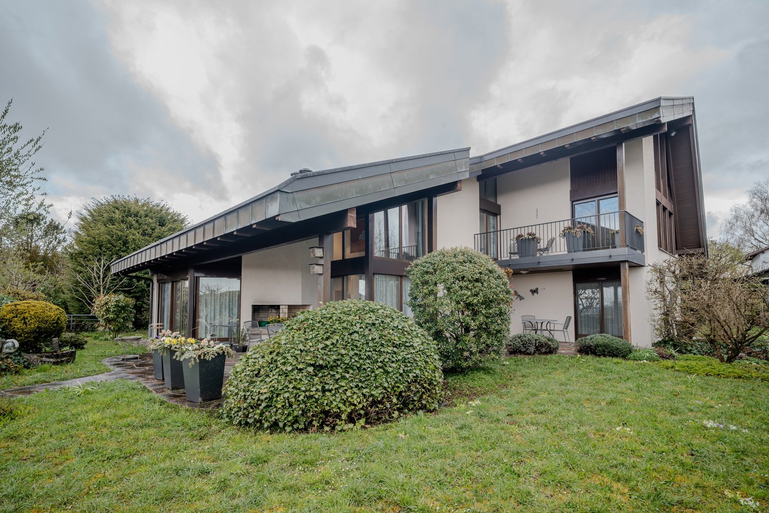 Modern house, white exterior, large windows, balcony, garden, shrubs, pathway