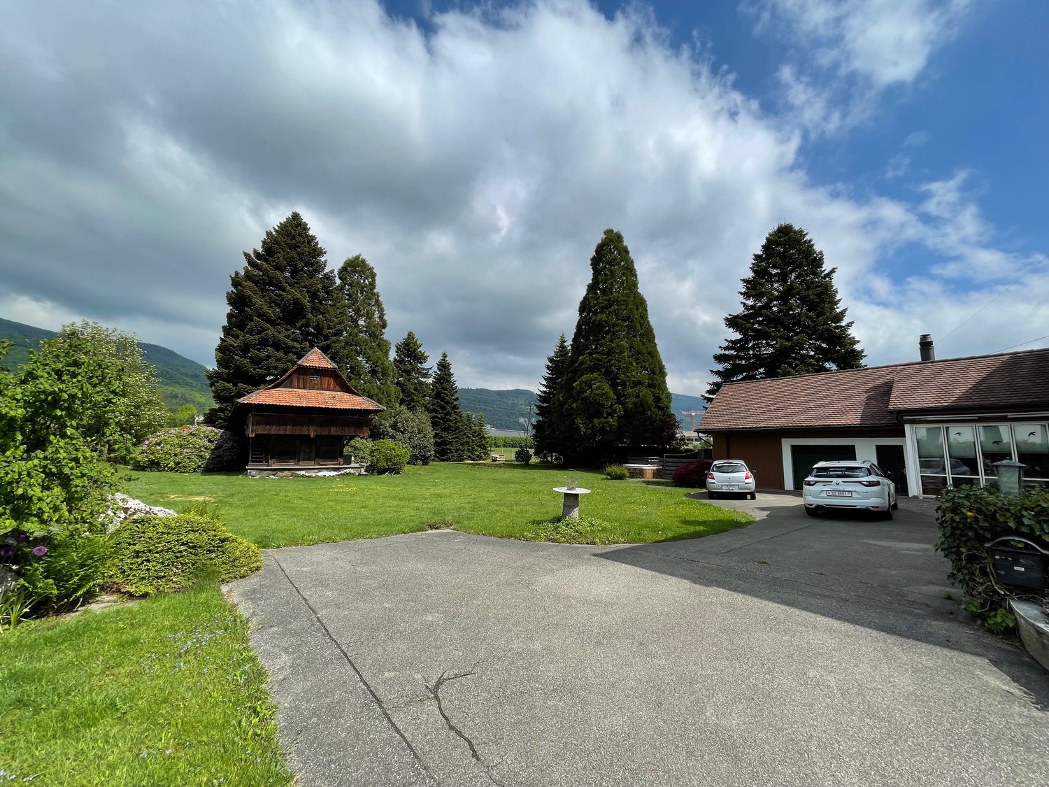 wide lawn, parked cars, detached house in the background, small wooden house, trees, mountains