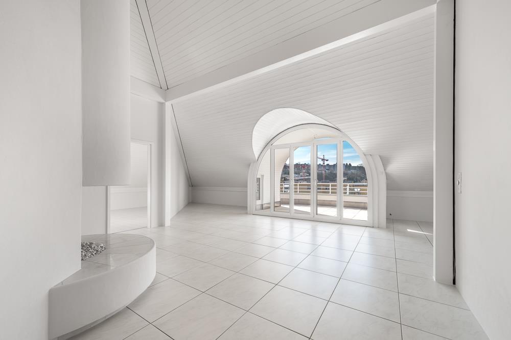 Spacious attic living room with white walls, large arched windows providing a view, and a tiled floor.