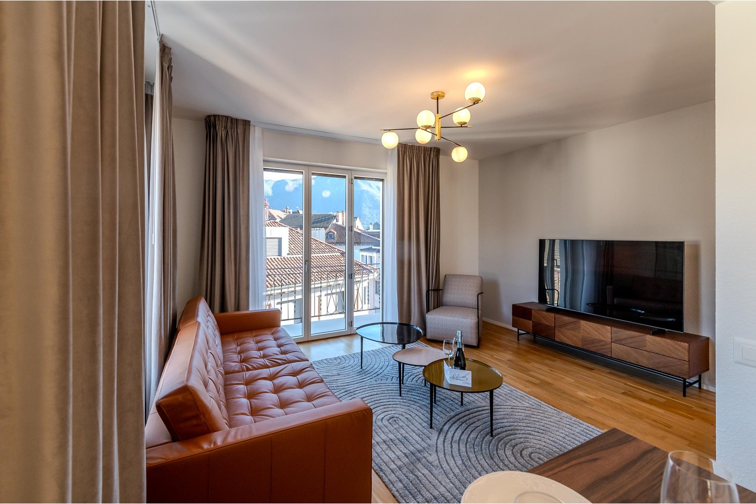 leather couch, coffee table, TV, armchair, chandelier, rug, balcony