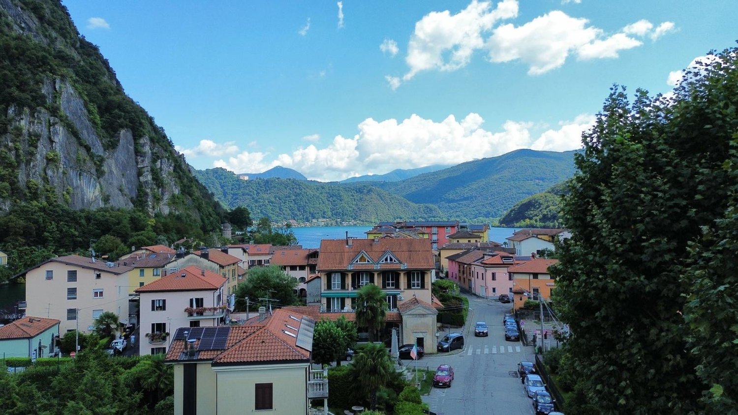 Mountain village with houses, solar panels, cars parked, lake, mountains