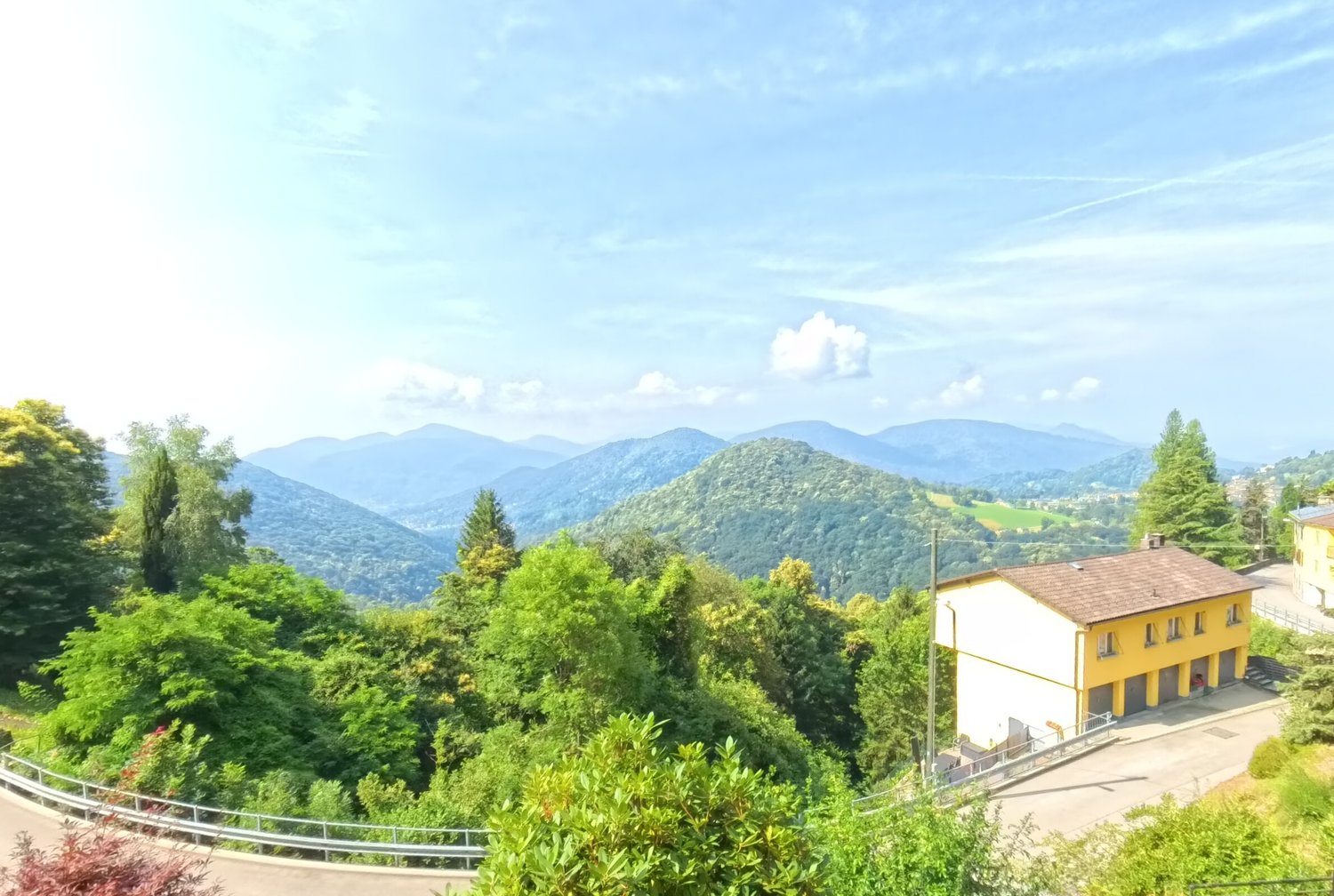 yellow house, brown roof, garage, surrounded by trees, mountains in the background