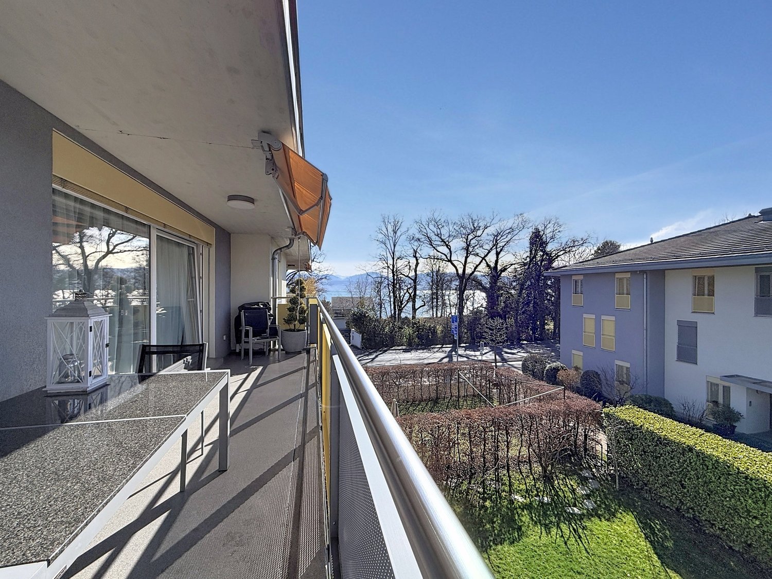 Balcony with glass railings, table, chairs, potted plant, awning, view of mountains and trees