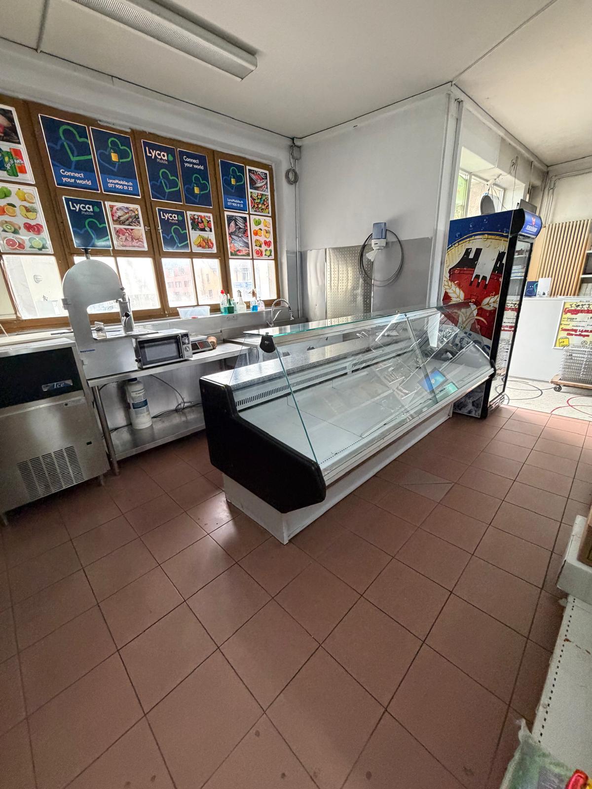 empty room with tiled floor, glass display case, microwave, refrigerator, and posters on the wall