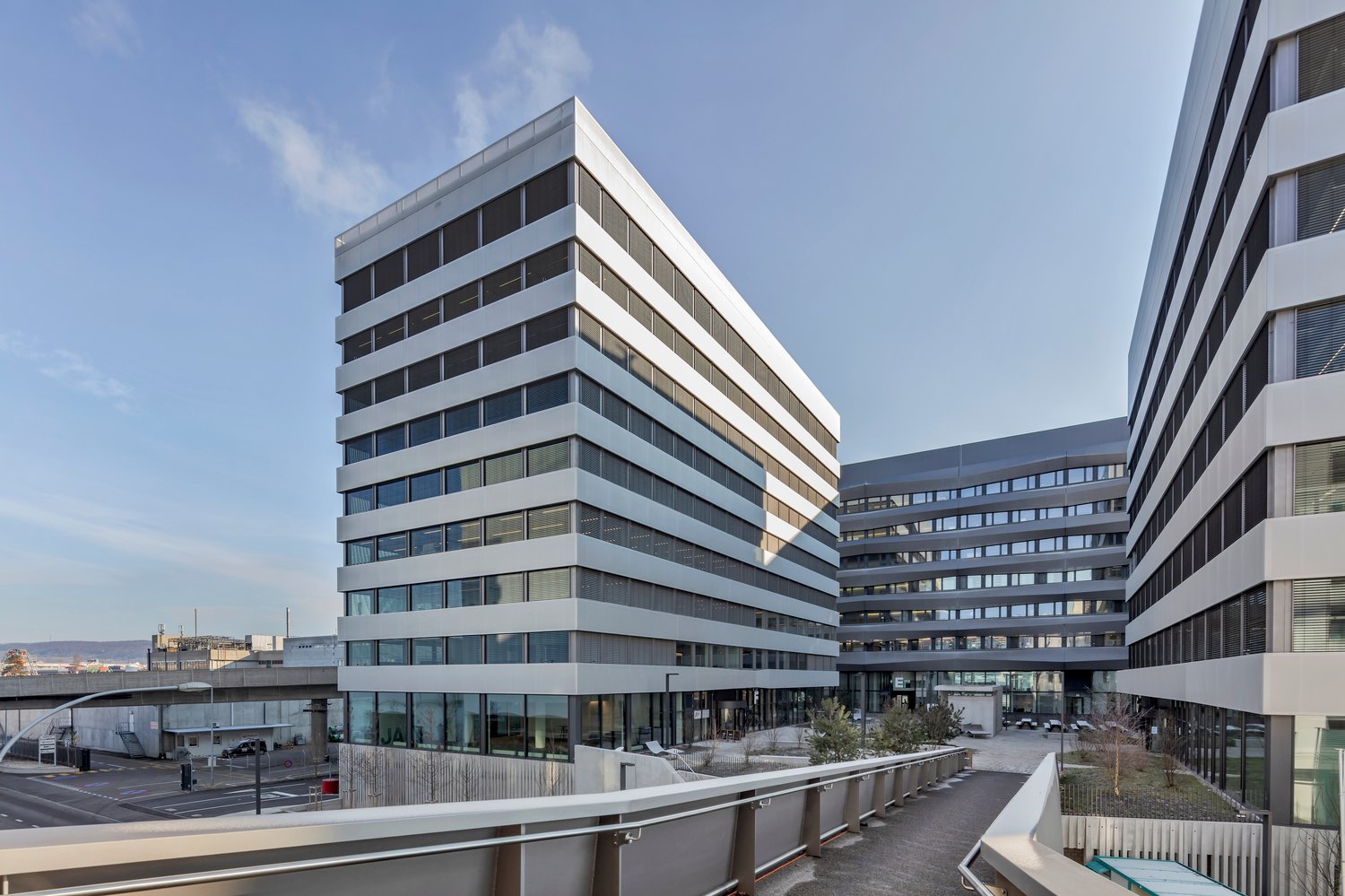 Modern office building with glass facade, multiple floors, and a landscaped area in front.