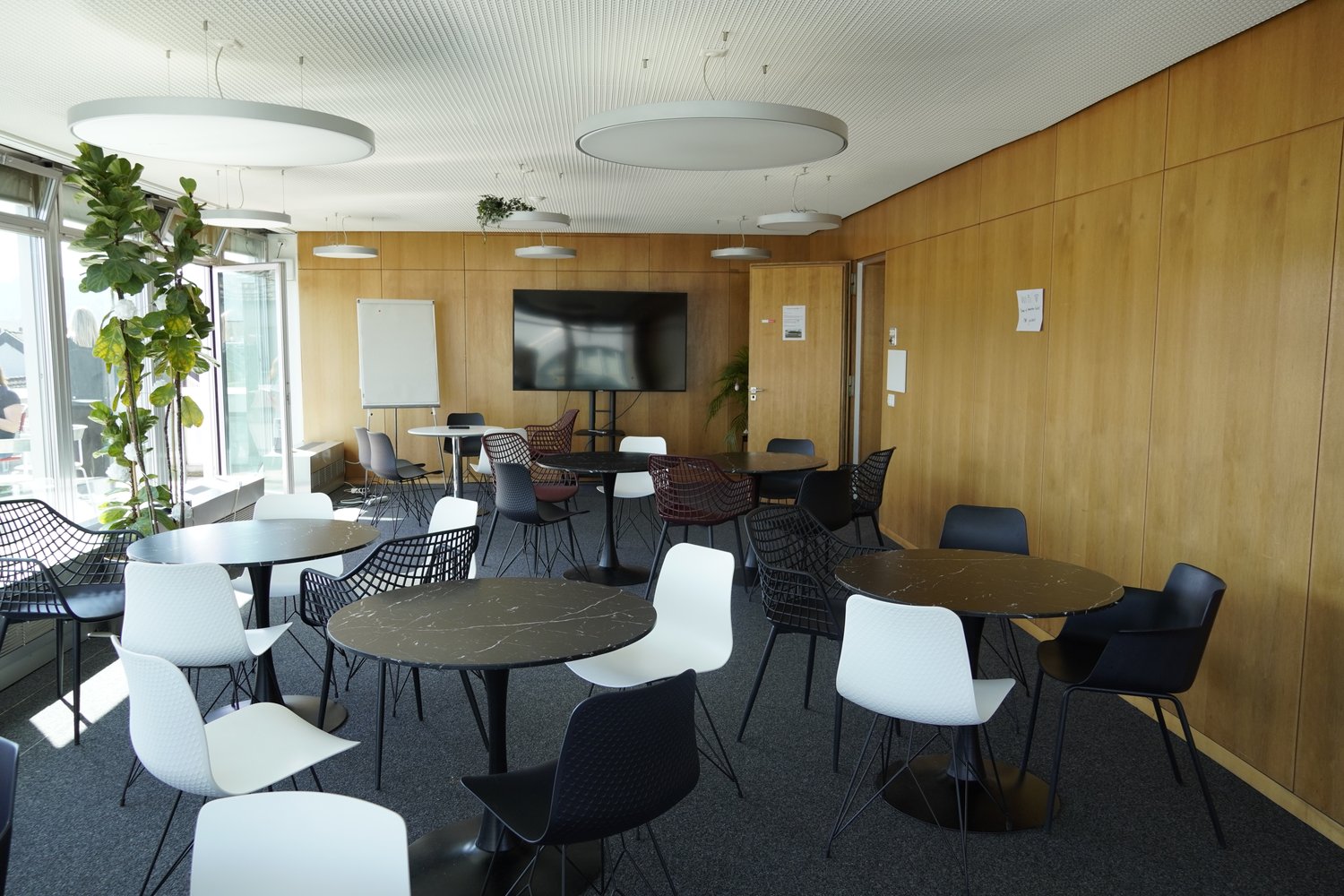 modern office room with round tables, chairs, wooden walls, large windows, whiteboard, TV