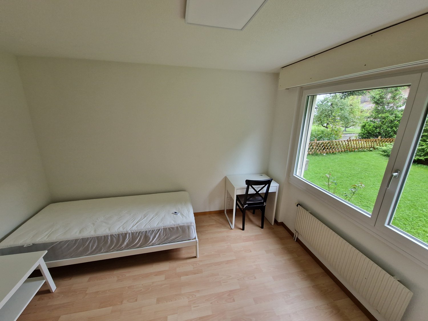 single bed, desk, chair, white walls, wooden floor, large window with outdoor view