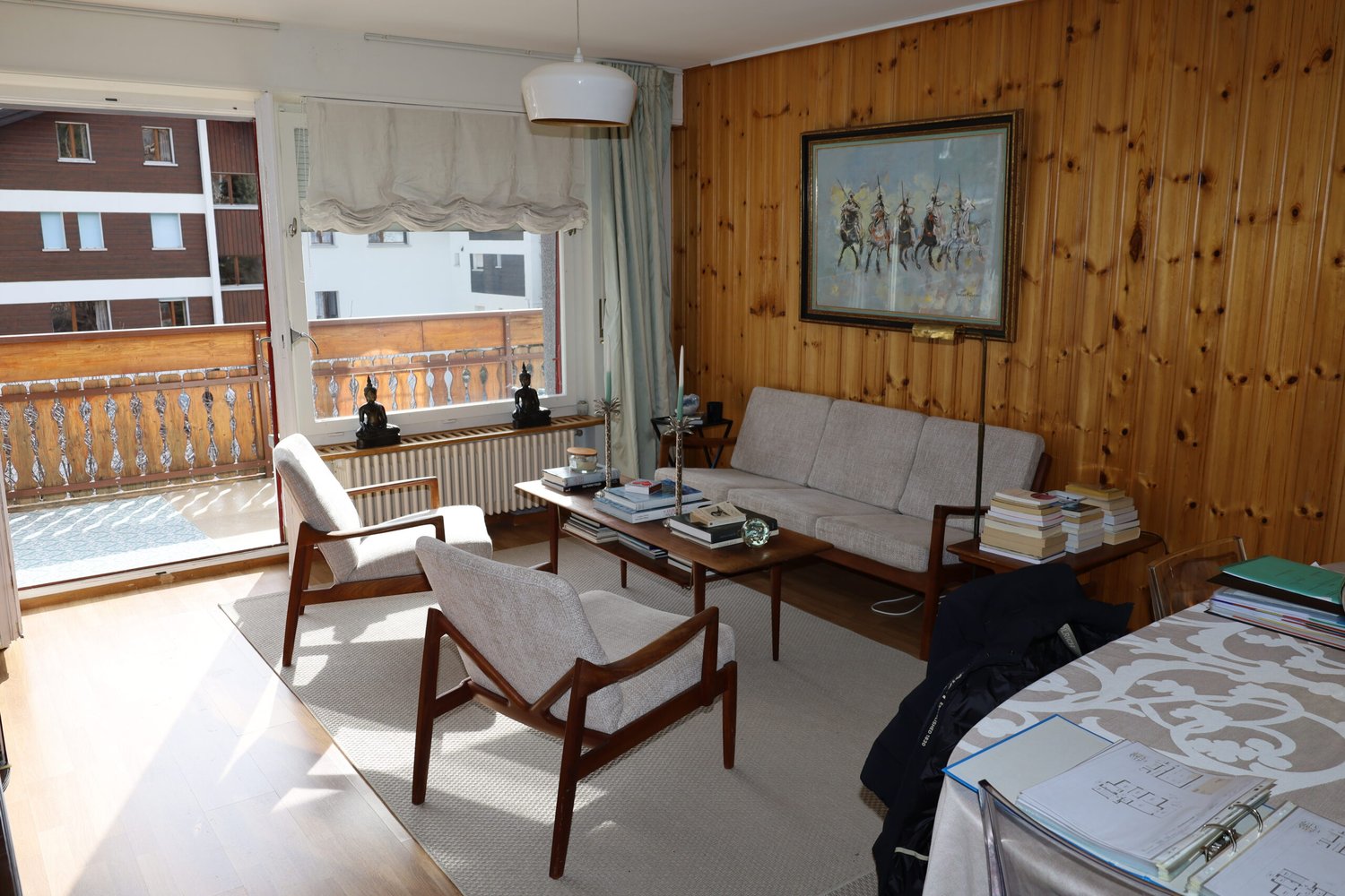 wooden walls, white rug, couch, chair, table with books, balcony, window with view