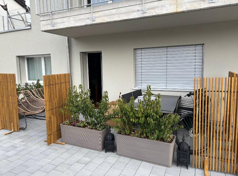 Wooden barriers with plants, tiled patio, patio furniture with plants, bicycle, white blinds, a window, an open doorway