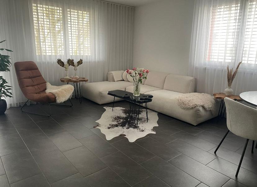 modern living room, white couch, modern black table, black tile flooring, white decorative curtains, white coffee table, large windows, two side tables, white rug, chair