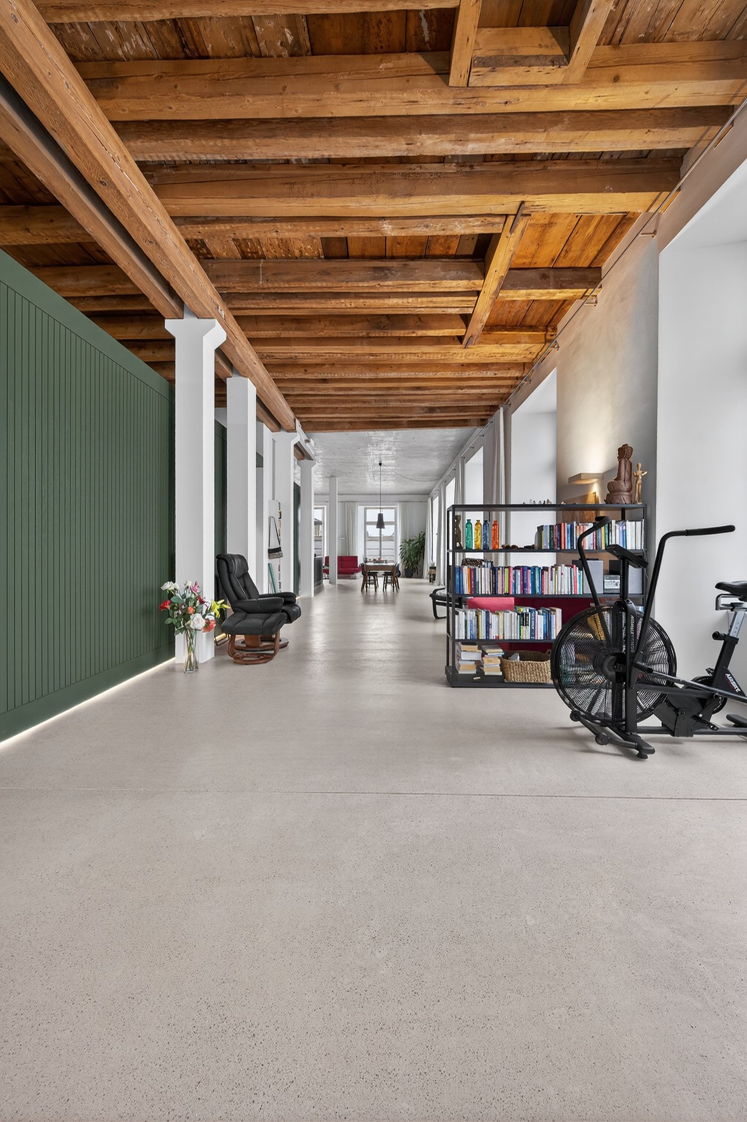 Open space with large wooden beams, white walls, white floor, green wall, living room items