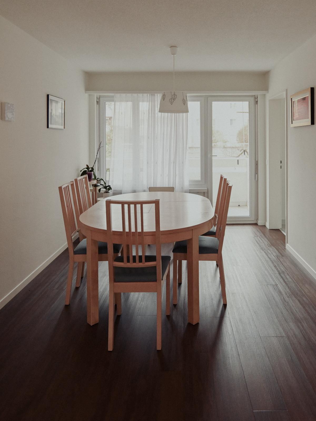 Dining room with wooden table, six chairs, wooden floor, and glass doors to a balcony