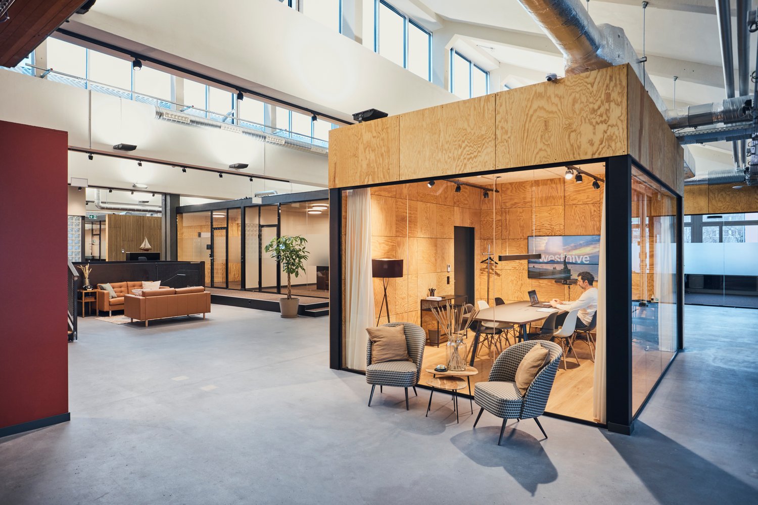 Open space office with wooden partition, glass wall, a couch, a coffee table, a plant, a table, and chairs.