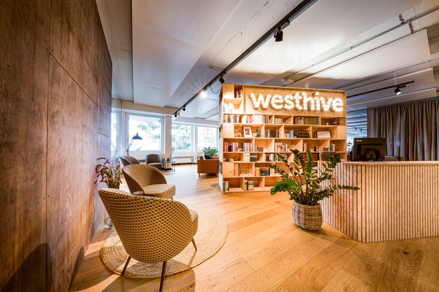large wooden bookshelves, wicker chairs, round rug, desk, green plants, wooden counter, glass walls, windows