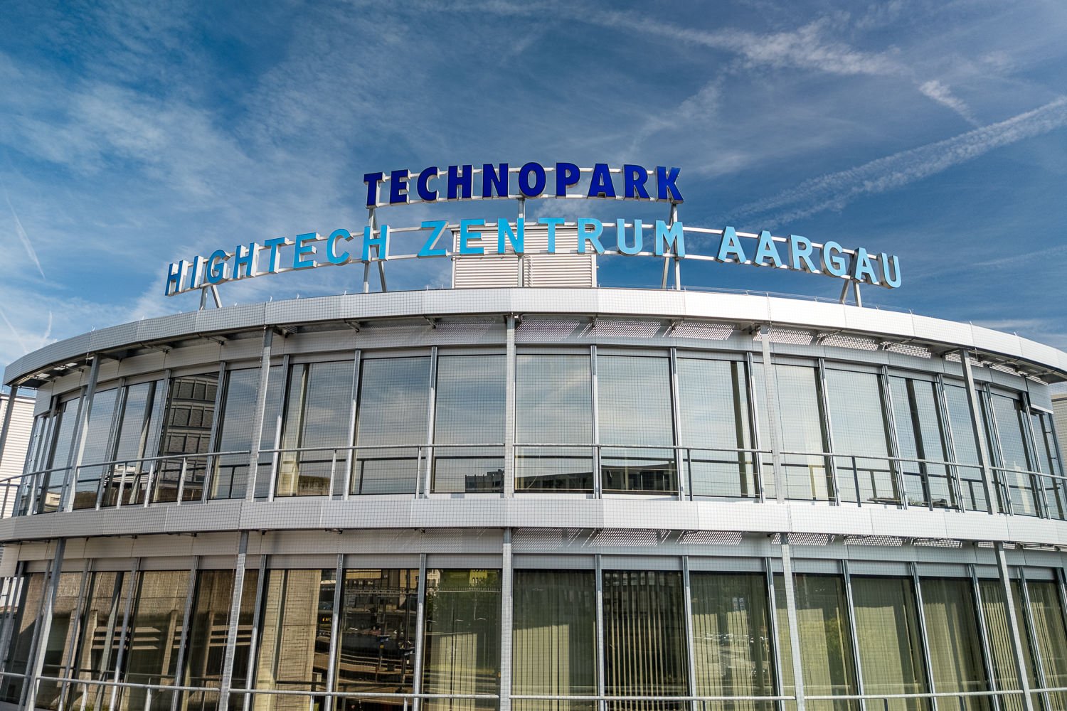 The image shows a large, modern building with a prominent sign that reads 'TECHNOPARK HIGHTECH-ZENTRUM AARGAU'. The building has a glass facade and appears to be a commercial or office space.