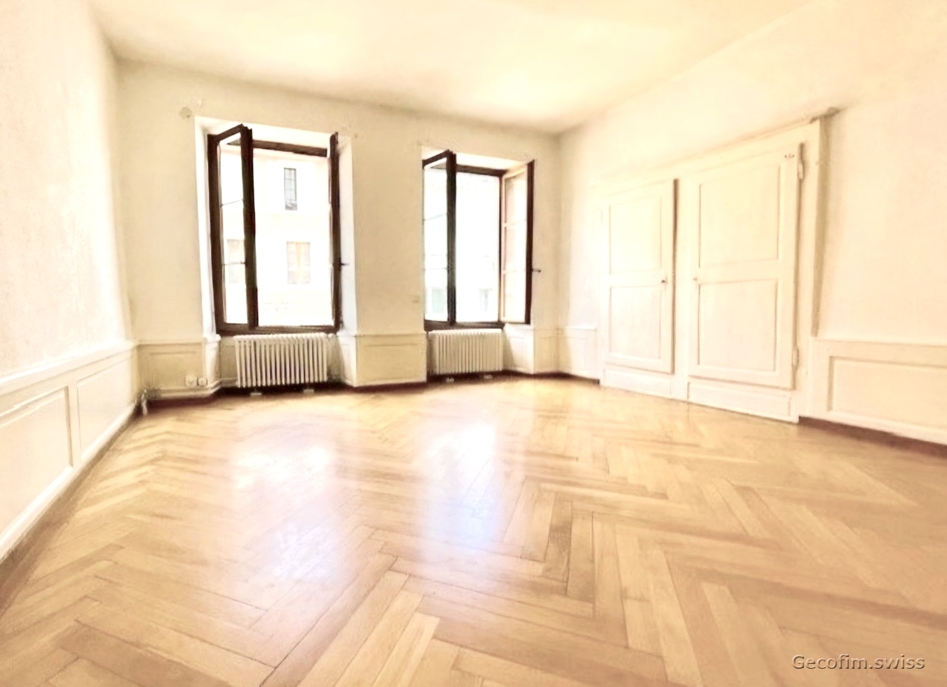 empty room, wooden floors, white walls, three windows, white doors, two white radiators