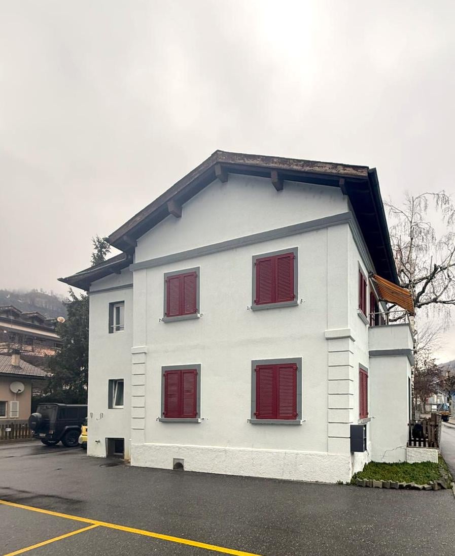 White two-story house, red shutters, beige awning, raised ground floor, entrance to the right