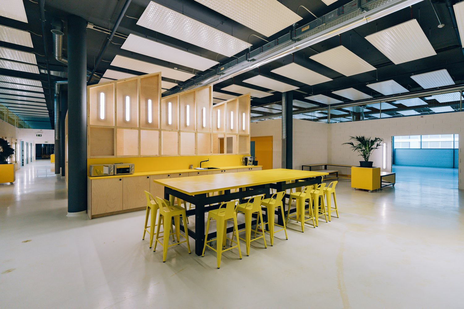 large open room with yellow counters and barstools, kitchen area with modern appliances, industrial style ceiling