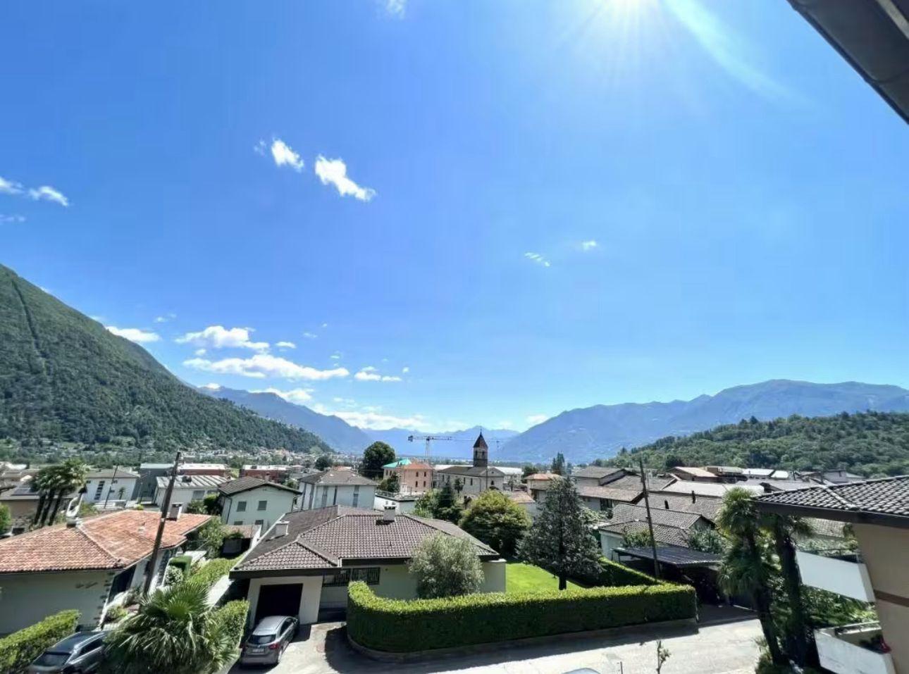 Town with mountains in the background, brick houses, tiled roofs, a car parked in front of one house, another car parked in a garage.
