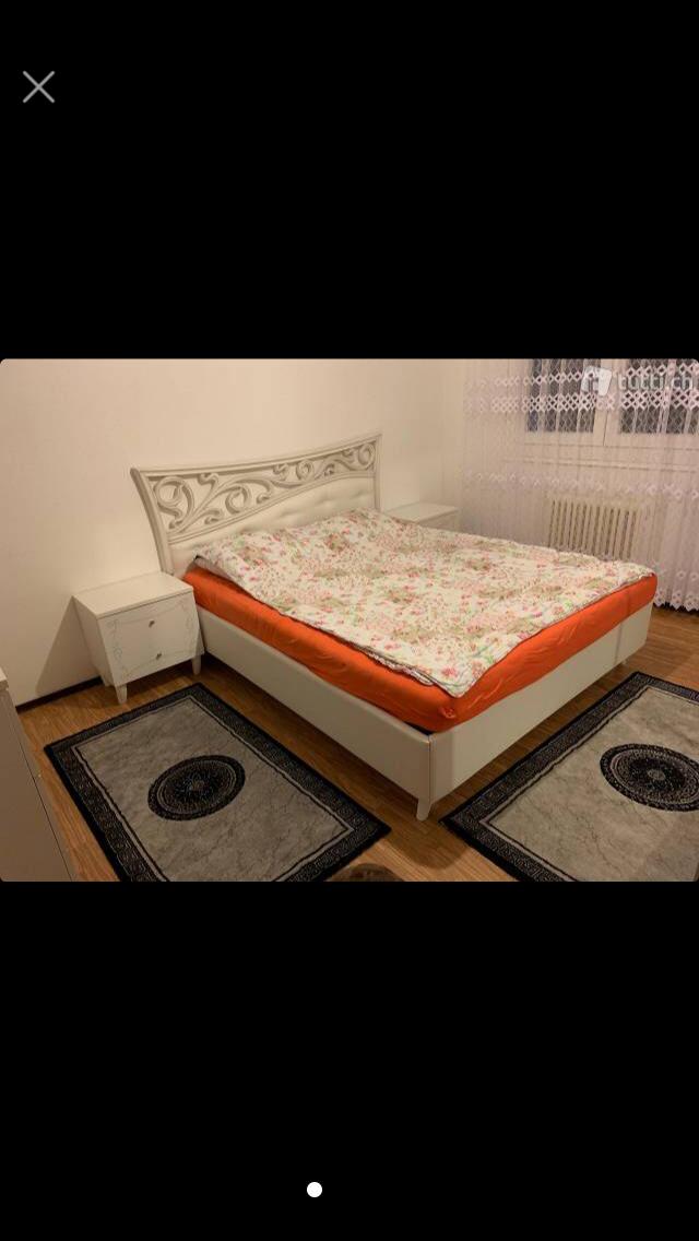 a bed with white headboard, white cabinet, and two rugs, white wall, window with curtains