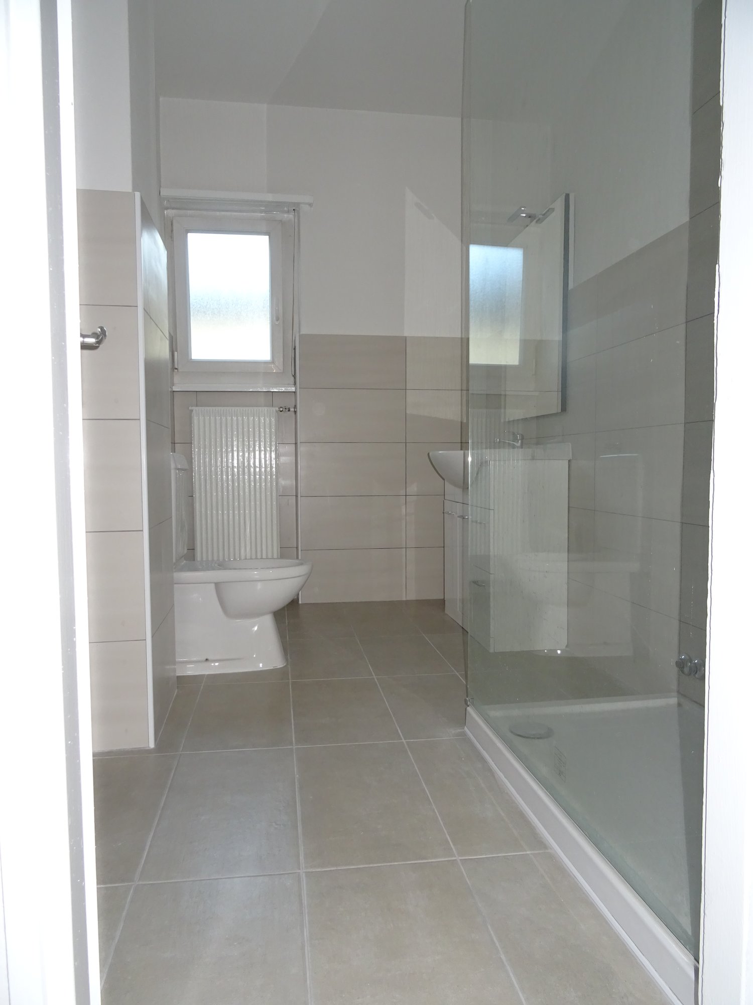 Bathroom with tile flooring, shower, sink, toilet, and a heater.