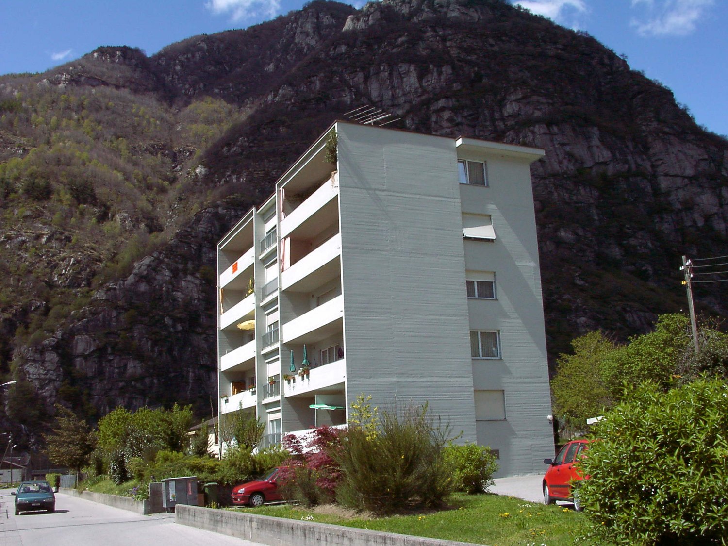 Multi-story building with multiple balconies, located at the base of a rocky mountain with steep slopes