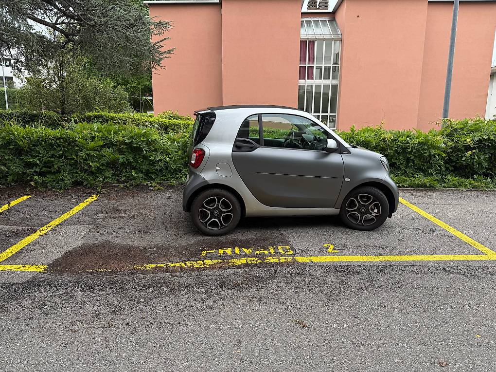 small silver car parked in parking lot in front of building