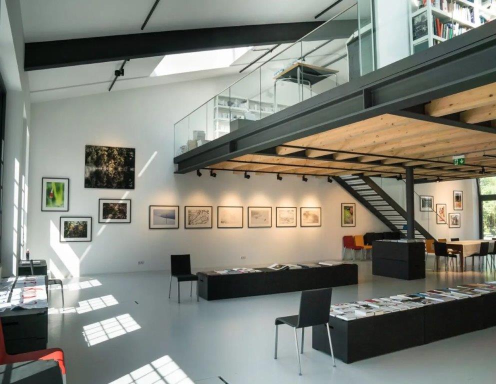 High ceiling, gallery-style space, glass railings, skylights, mounted pictures, furniture in a neat manner