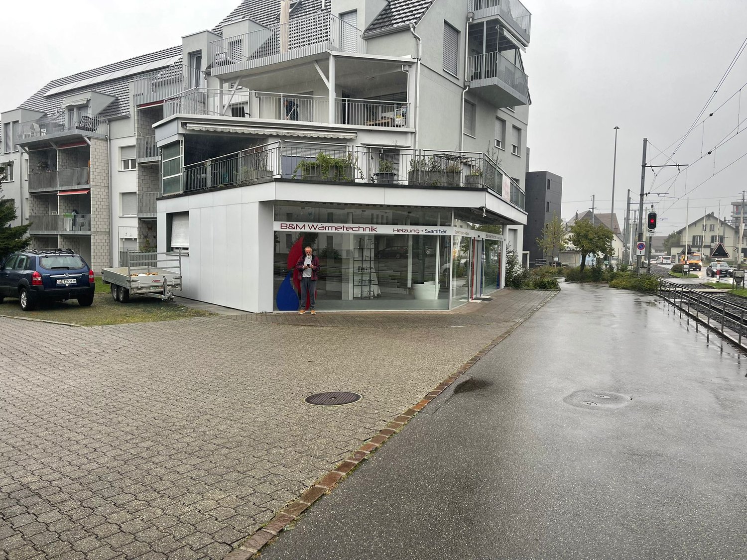 An apartment building with several floors and a storefront at the ground floor, with a car parked in front of it.