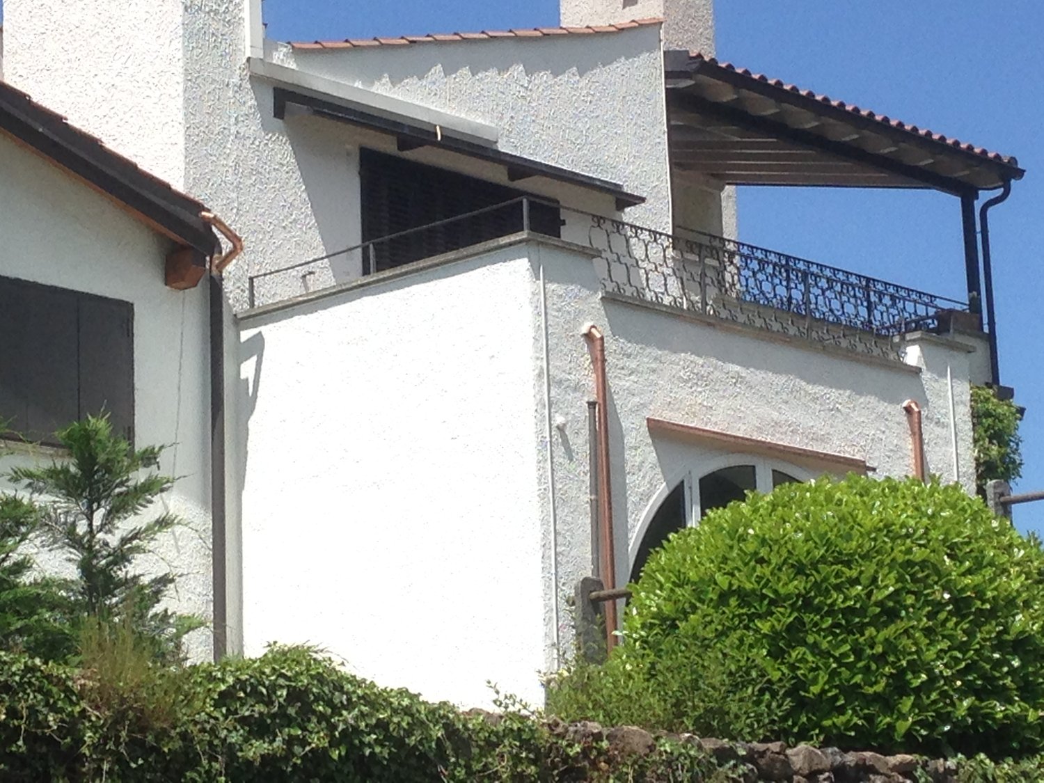 White stuccoed house, covered balcony with metal railings, chimney, metal guttering, glass window