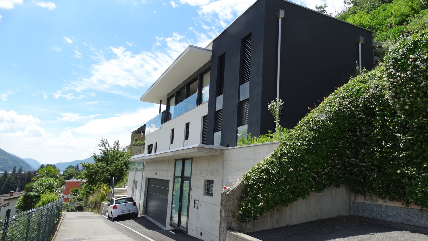 Modern house, black and white exterior, large windows, garage, concrete wall, greenery
