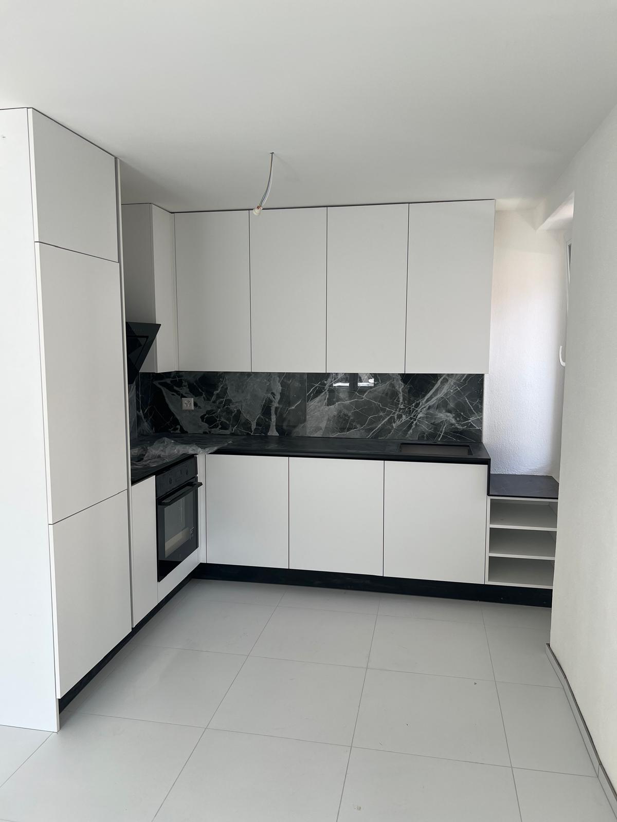 modern kitchen with white cabinets, black marble countertop, white tiled floor, built-in oven, sink, and shelves