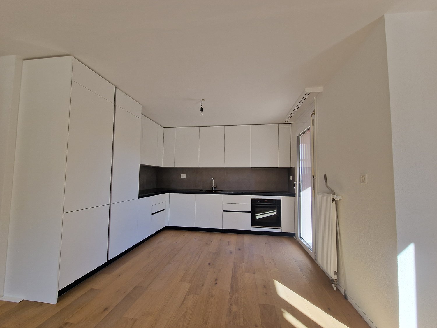 modern kitchen with white cabinets, wooden floor, black countertops, stainless steel sink, built-in oven, sliding glass door