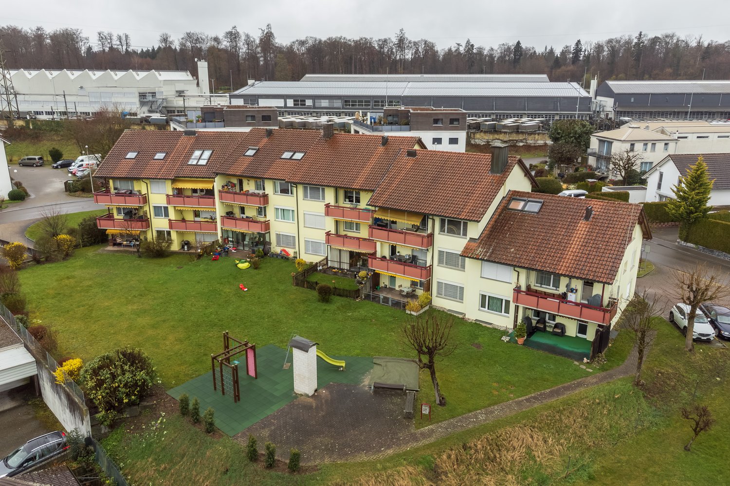 Apartment complex with yellow exterior walls, brown roofs, balconies, and playground in the front.