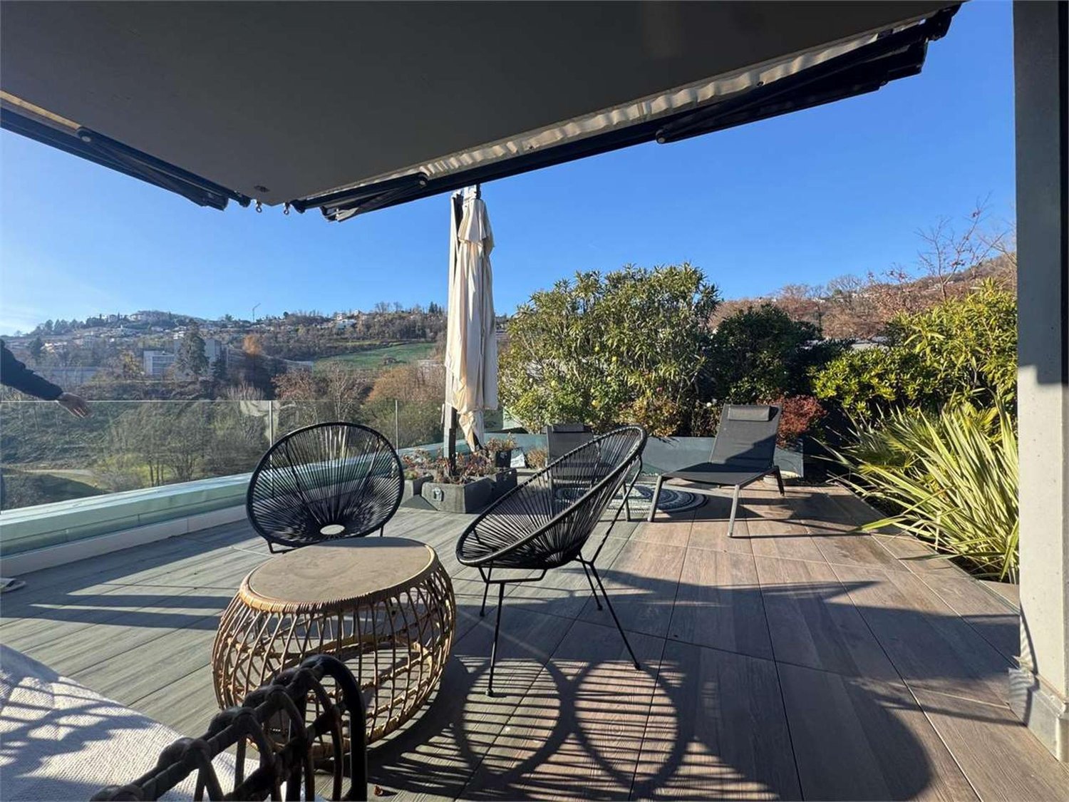 Wooden deck with outdoor furniture, glass railing, plants, and a view of the landscape