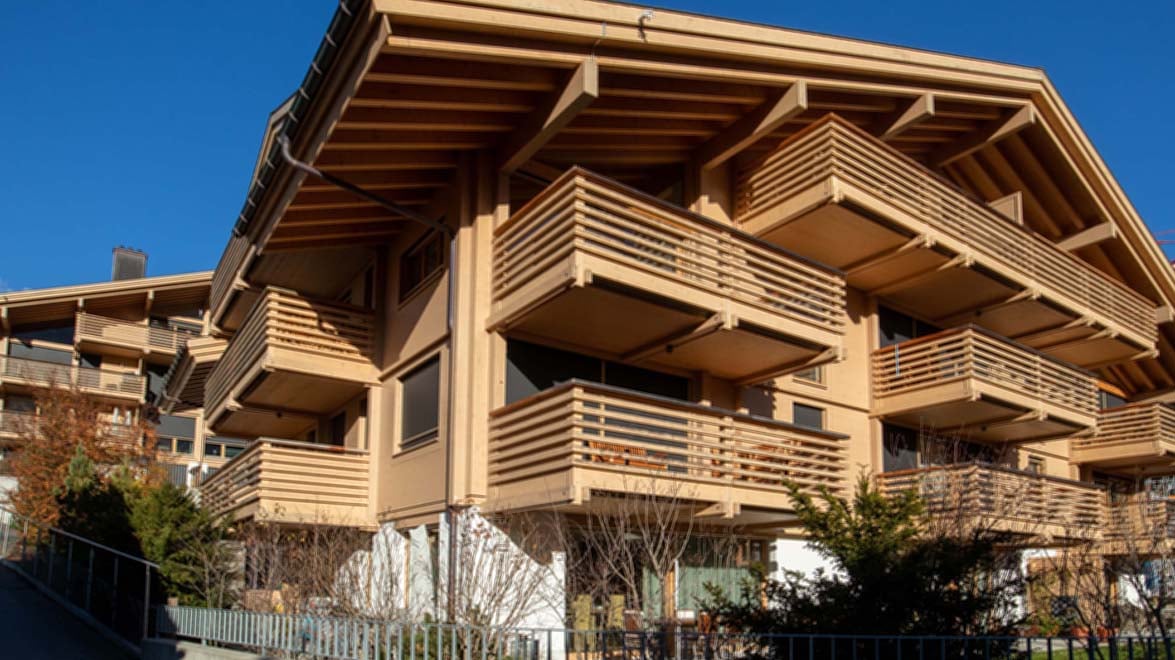 Modern wooden apartment building with multiple balconies, large windows, and a sloped roof