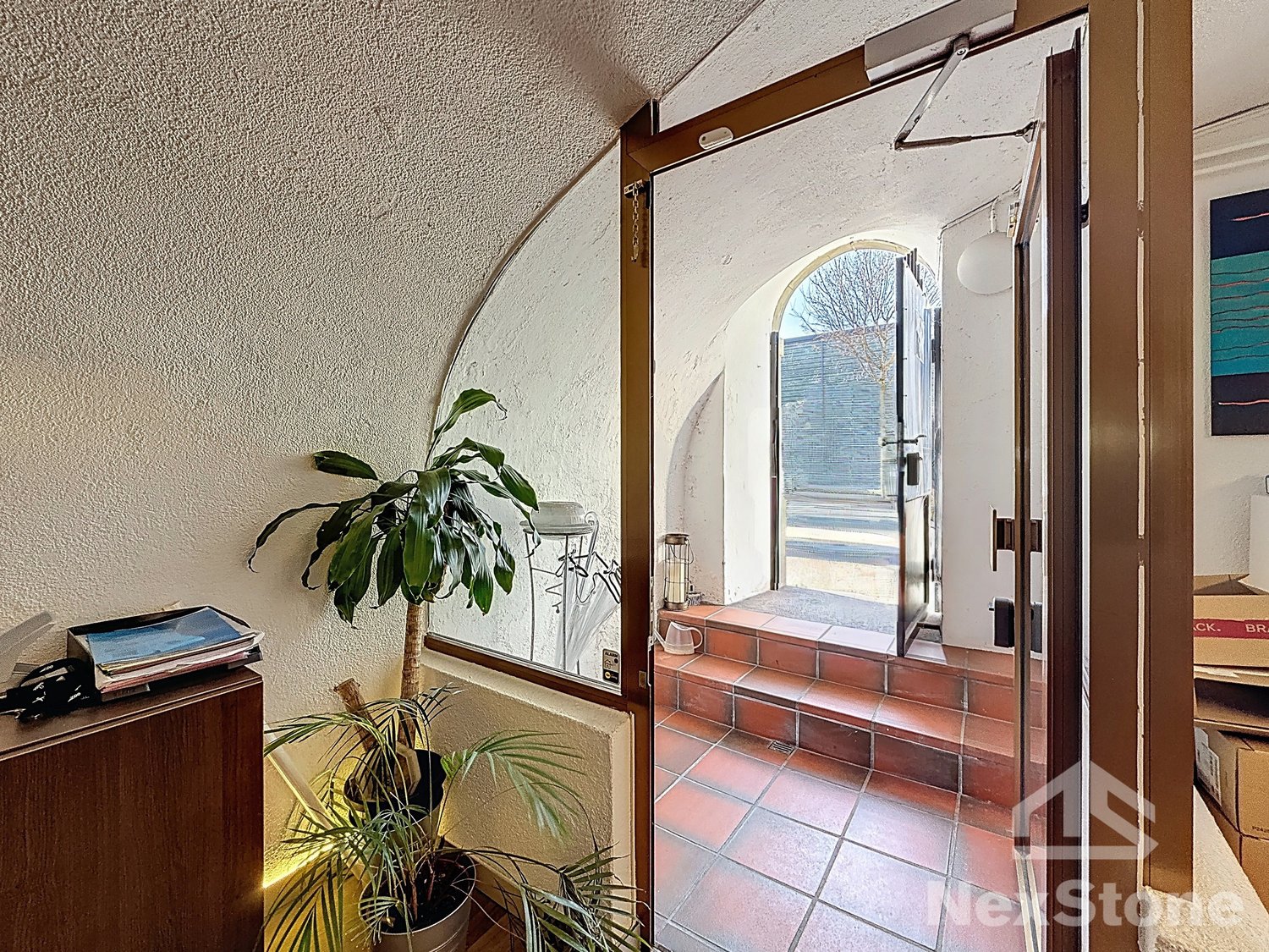 open door, arched window, red tiled floor, plants, wooden cabinet, open door leading to outside