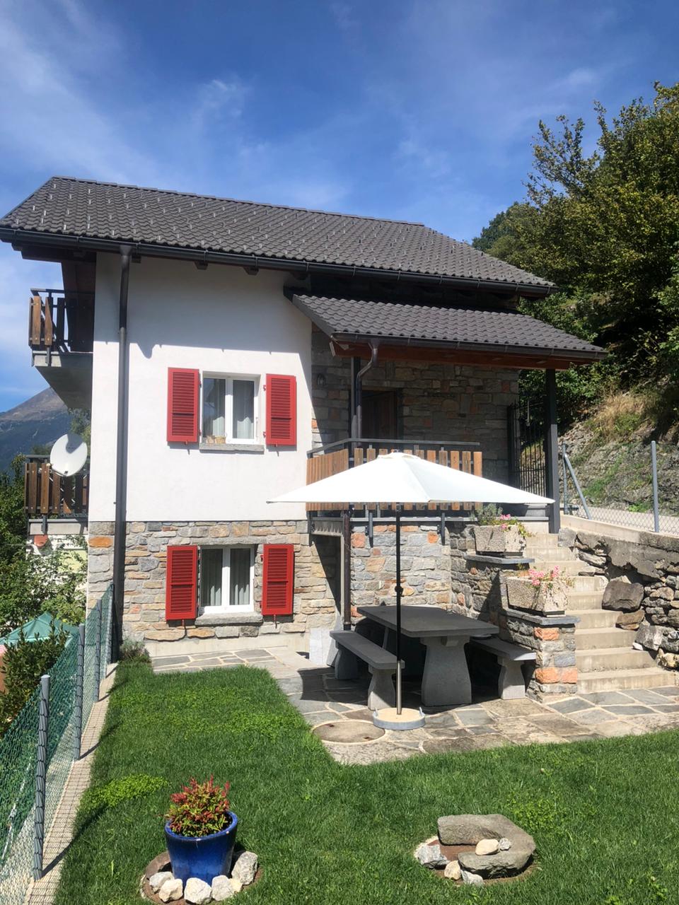 2 story house, white and red shutters, stone wall, balcony, outdoor table, umbrella, garden, lawn