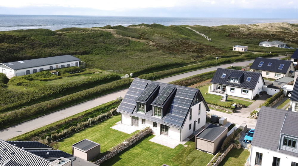 Modern house with solar panels, surrounded by green landscape, sea view