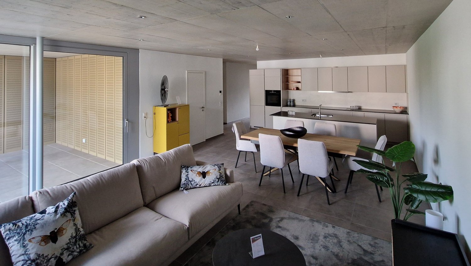 Open plan living and dining area with modern furniture, large windows, and a yellow storage unit.