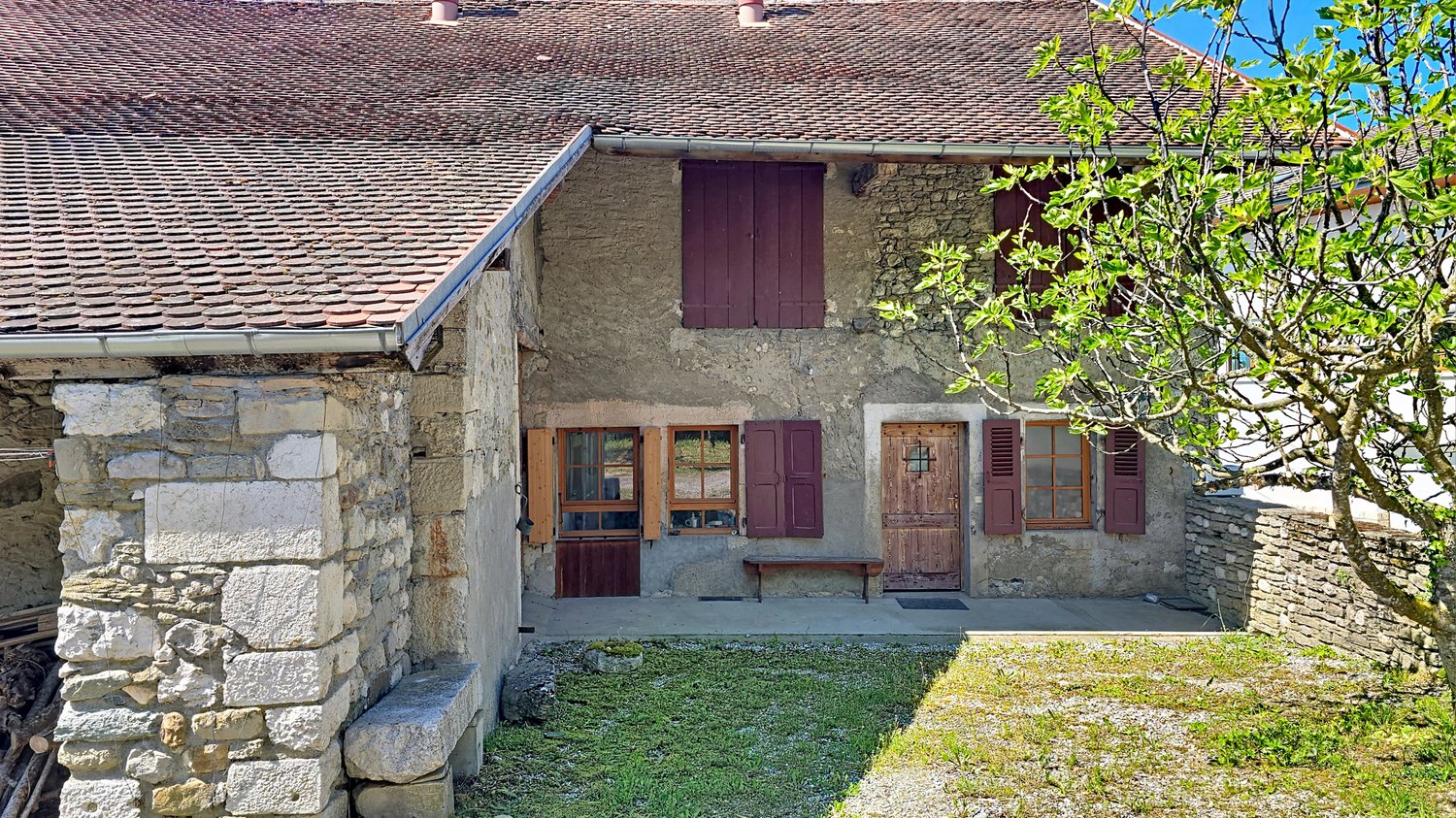 Stone house, brown roof, wooden doors, wooden shutters, wooden bench, stone wall, grassy area