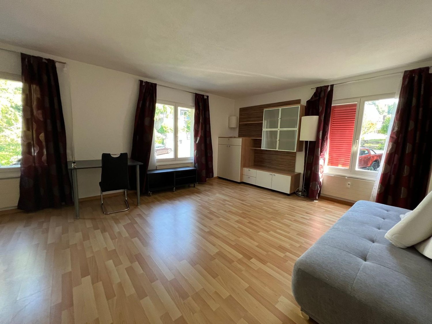 Spacious living room with hardwood flooring, white walls, large windows, a sofa, a coffee table, and a TV stand with storage units.