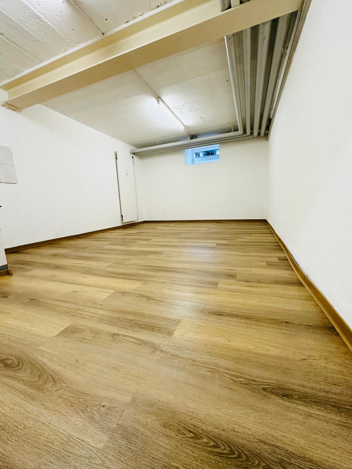 empty room, hardwood floors, white walls, small window on the back wall, a door on the left side