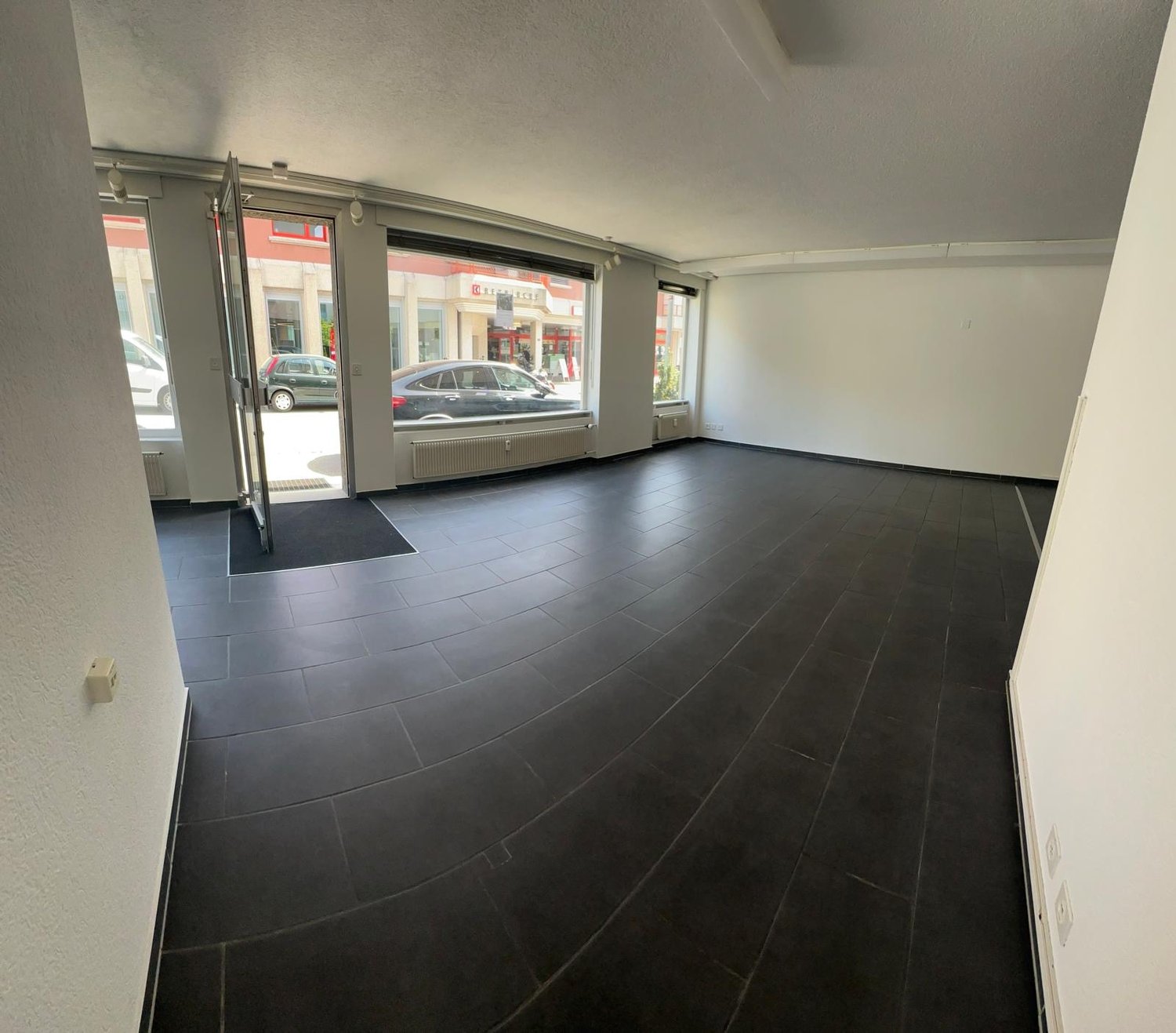 Large open commercial space with black tile flooring, large windows overlooking the street, and a glass entrance door.