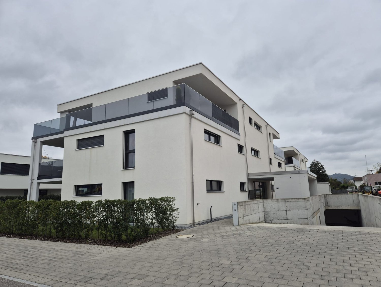 Modern 2-story building, white facade, glass balconies, paved driveway, garage