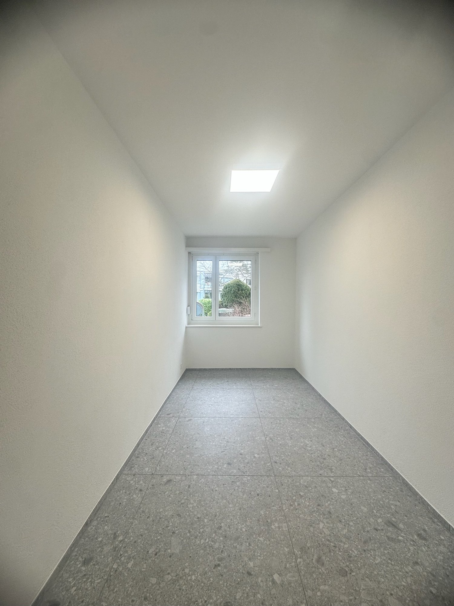 Empty room with white walls, a large window, and a gray terrazzo floor.