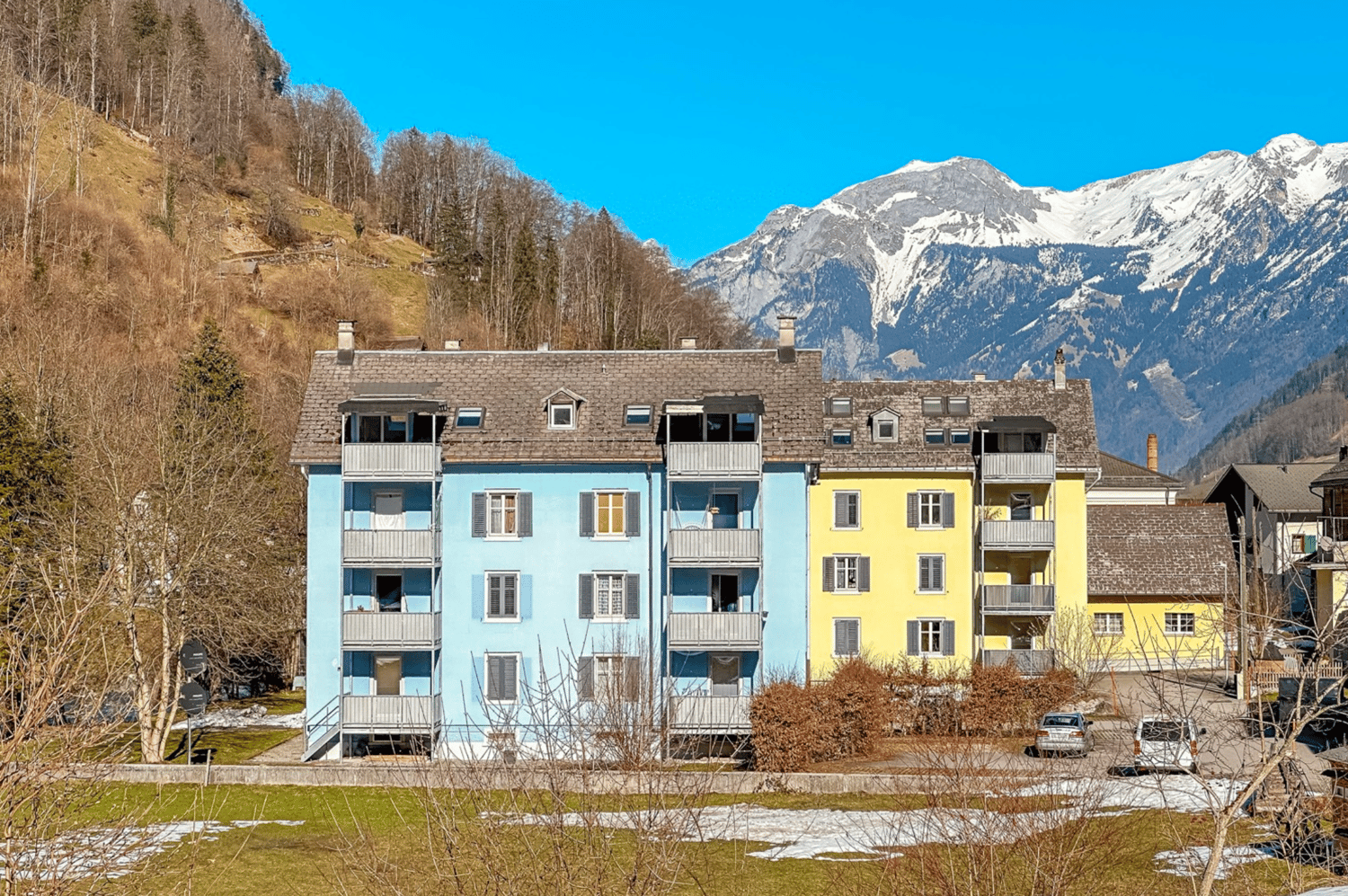 Multi-story apartment building with colorful facades, balconies, and surrounded by mountains and trees