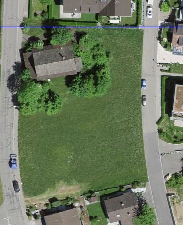 Aerial view of a residential area with a large green field, several houses, and parked cars.