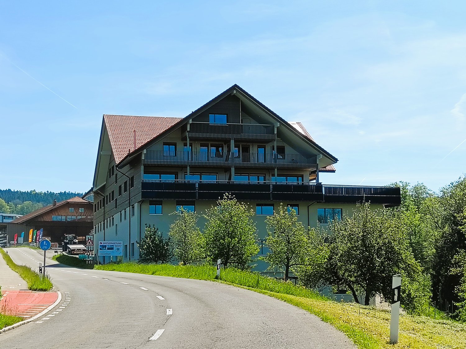 2 story building, with red roof, blue windows, balconies, parked vehicle